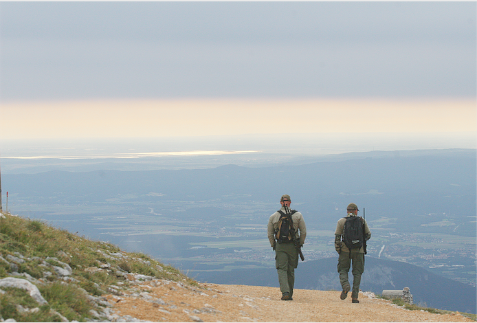 Zwei Jäger gehen über einen Hügel in die Entfernung.