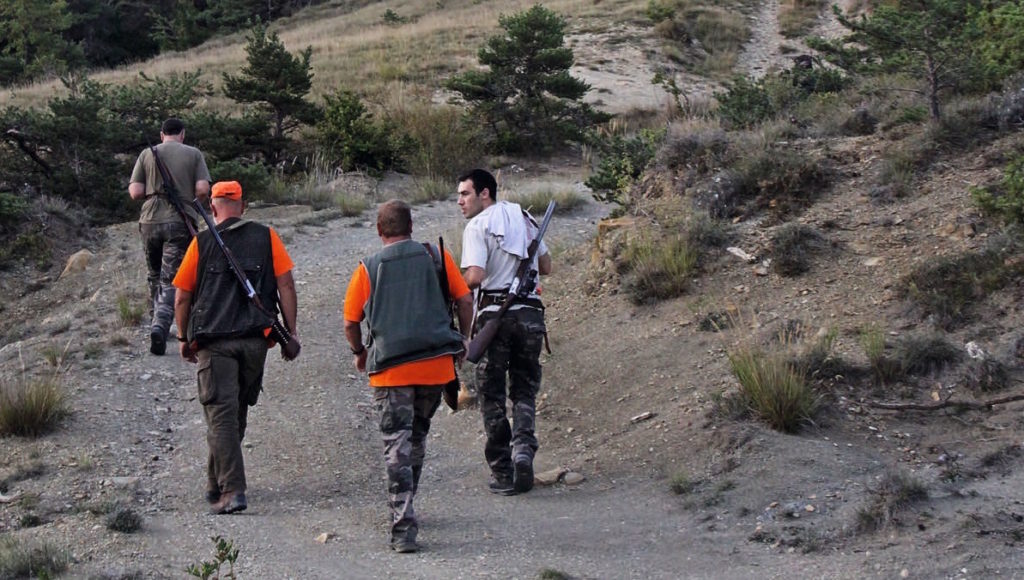 Vier Jäger steigen auf den Berg entlang des dunklen Schotterpfads.
